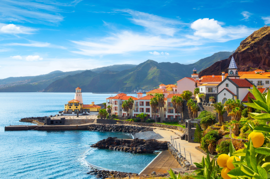 Blick auf eine Bucht auf Madeira, links das Meer, rechts Häuser und Berge, grün bewachsen